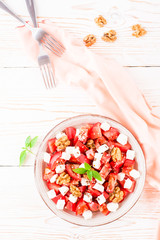 Fresh appetizer of tomatoes, feta cheese, walnuts, flax seeds and sesame seeds in a plate on a white wooden table. Top view