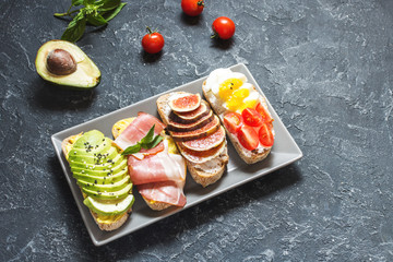 A set of avocado sandwiches, cherry tomatoes and eggs, figs, prochutto on a stone background.