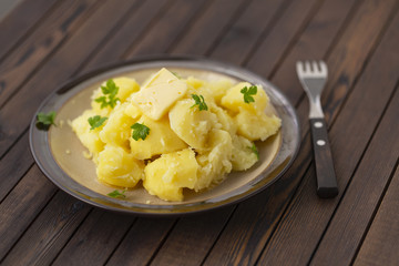 Boiled potatoes with fresh herbs and oil in a bowl on a wooden table