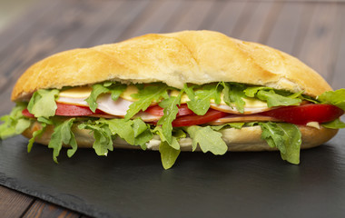 Baguette sandwich with ham, tomatoes, cheese and arugula lettuce. Delicious Breakfast or snack. Close up