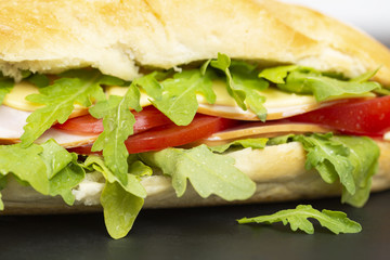 Baguette sandwich with ham, tomatoes, cheese and arugula lettuce. Delicious Breakfast or snack. Close up