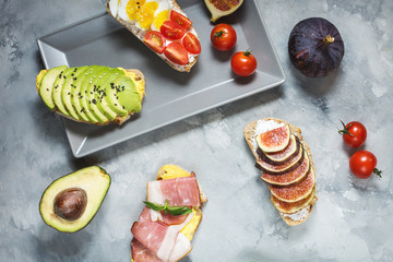 A set of avocado sandwiches, cherry tomatoes and eggs, figs, prochutto on a concrete background