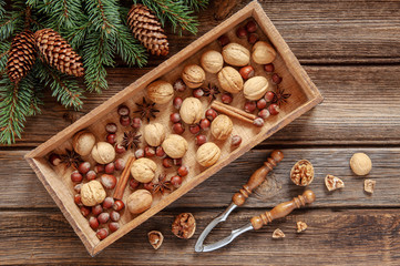 Christmas background with fir tree branches, cones, mixed nuts and spices in wooden box and nutcracker. Top view, close up on vintage wooden table