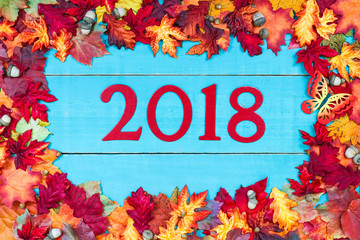 Year 2018 in bold red hanging on antique rustic teal blue wood background with colorful autumn leaves border