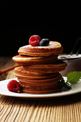 Pancakes with berries and maple syrup on rustic table