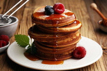 Pancakes with berries and maple syrup on rustic table