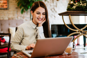 Attractive young woman working on laptop at cafe. Freelance work.