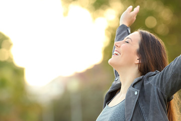 Happy lady breathing fresh air raising arms in a park