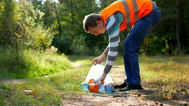 male volunteer cleaner in the signal orange vest cleans garbage in the forest, cleansing the forest and nature from garbage, garbage and nature, rubbish