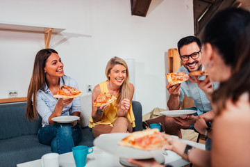 Group of friends laughing while eating pizza at home.