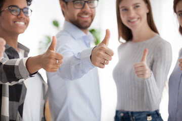 Happy multiracial millennial diverse business people or students standing together in a row smiling showing thumbs up, close up focus on hands. Successful teamwork collaboration and approval concept