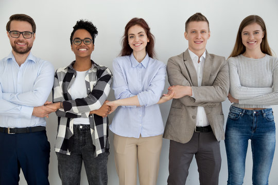 Five cheerful diverse multiracial millennial businesspeople students holding hands standing opposite wall smiling and looking at camera. Team building unity support teamwork or common goal concept