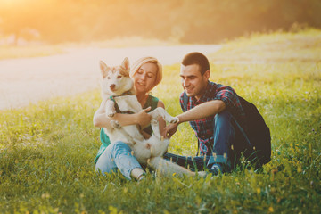 Dog with owners spend a day at the park. Young couple and husky running, playing and having fun.