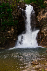 Fototapeta premium Running Eagle Falls in Glacier Nation Park. Running Eagle Falls is named after a female warrior of the Amskapi-Pikuni Native American people. This is a double water fall with both falls flowing in t