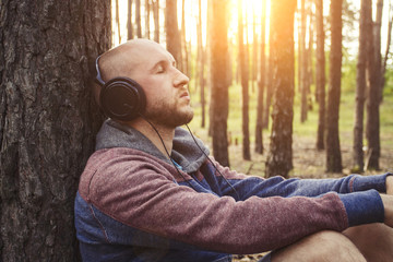 Man in headphones is sitting in a forest with his back to a tree. Concept of outdoor recreation and...