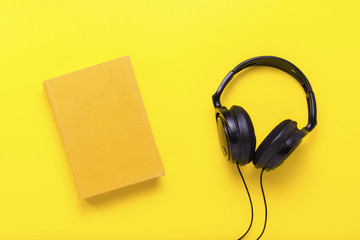 Book with a yellow cover with text English and black headphones on a yellow background. Concept of audio books, self-education. Flat lay, top view