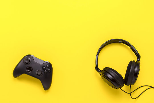 Black headphones and a gamepad on yellow background. Concept of the game on the console or computer. Rest after work. Cybersport. Flat lay, top view
