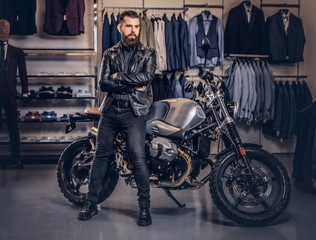 Fototapeta na wymiar Brutal male dressed in black jacket leaning on a retro sports motorbike at the men's clothing store.
