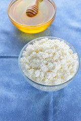 Cottage cheese. Cottage cheese and honey on blue napkin. Soft cheese in glassware. Dairy product for breakfast. Copy space