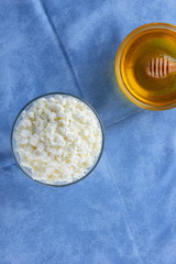 Cottage cheese. Cottage cheese and honey on blue napkin. Soft cheese in glassware. Dairy product for breakfast. Copy space