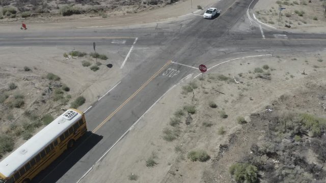 Aerial shot of a Yellow American school bus turning on to a Street into the Sandy California Desert