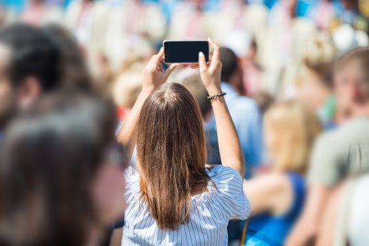 Young woman with smartphone in a hand taking picture in crowd of people