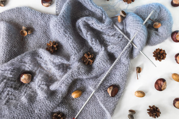 Grey knitwork with needles and yarn balls with chestnuts, pinecones, acorns. Autumn cozy background.
