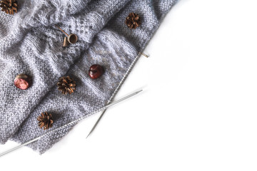 Diagonal grey knitwork on needles with chestnuts, pinecones on a white background, place for text. Autumn cozy background with copy space.