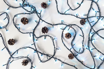 Tiny bright blue fairy lights and cones on a white background, top view. Festive background.