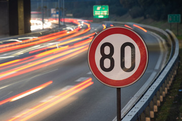 Long exposure shot of traffic sign showing 80 km/h speed limit on a highway full of cars in motion...