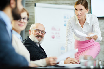Young confident businesswoman with paper discussing data with one of colleagues at seminar