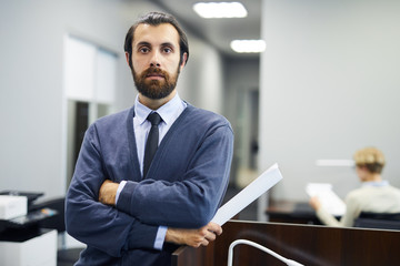 Naklejka premium Young elegant serious businessman looking at camera while standing by tribune in conference hall or auditorium