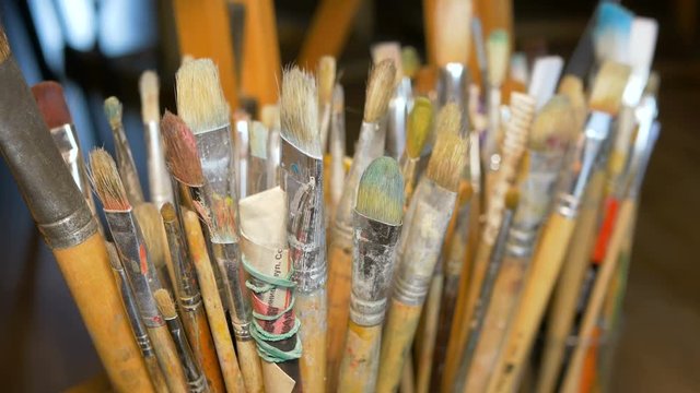 A lot of different paint brushes stand upright in vases. Professional equipment of the artist. Art Studio. Focus of the camera moves by objects.