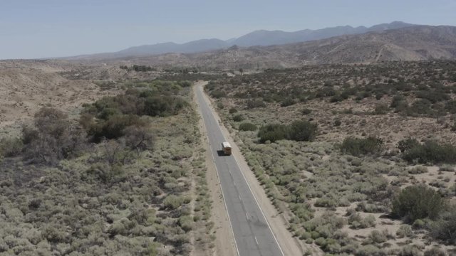 Aerial shot of a Yellow American school bus driving down a Street in the Sandy California Desert