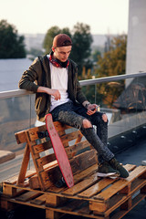 Young handsome man listening music in headphones and using smartphone on the rooftop of industrial building at the sunset.