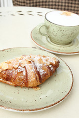 A cup of latte coffee and a croissant in a summer cafe on the table