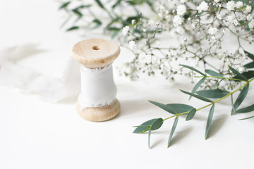 Feminine floral scene. Close-up of spool of silk ribbon, Eucalyptus parvifolia leaves and babys...