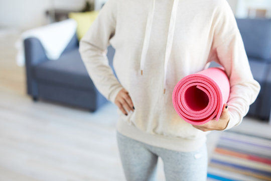Rolled pink mat held by sportswoman in light activewear before home workout