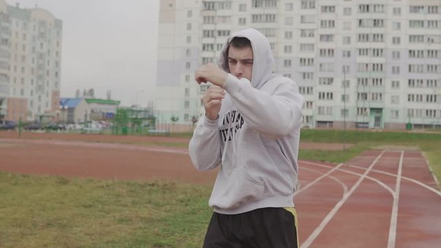 Portrait of man boxing with invisible opponent. Young man training at stadium in morning. Active male boxer in hoodie outdoors at stadium. Shadow fight. Vovinam Viet Vo Dao - kind of martial art