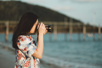 Young asian woman holding vintage camera with beach view in sunset light.