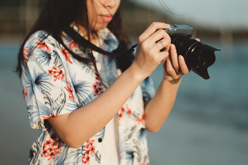 Young asian woman holding vintage camera with beach view in sunset light.