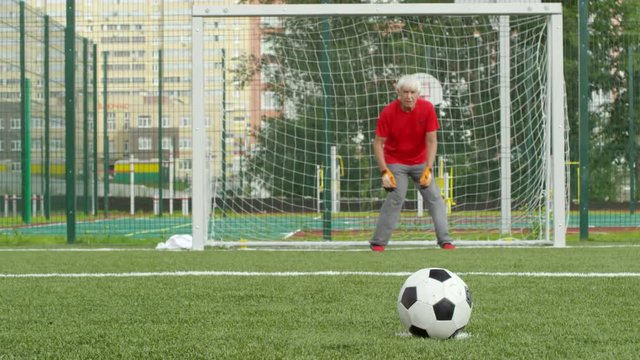 Senior man in sports clothing putting football on ground, then his teammate kicking it and scoring goal, tracking shot