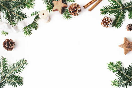 Christmas festive styled stock composition. Decorative floral frame. Fir tree branches border. Pine cones, wooden stars, cinnamon and ribbon on white wooden background. Flat lay, top view. Copy space.