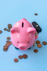 Top/front view of pink piggy bank with hammer and coins on blue background.