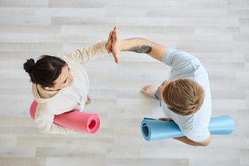 Active young man and woman with rolled mats giving high five to each other after sports training