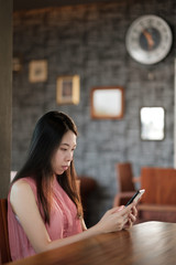 Young asian woman using mobile phone in modern style office on wooden table.