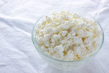 Cottage cheese. Cottage cheese on white background. Soft cheese in glassware on white napkin. Dairy product for breakfast. Copy space