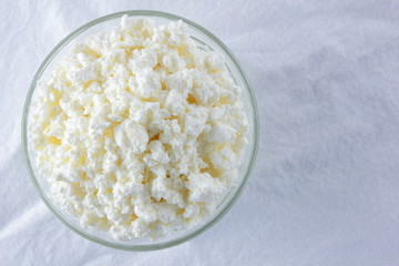 Cottage cheese. Cottage cheese on white background. Soft cheese in glassware on white napkin. Dairy product for breakfast. Copy space