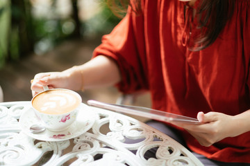 Woman holding tablet computer and coffee cup in coffee shop.