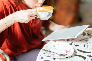 Woman holding tablet computer and coffee cup in coffee shop.